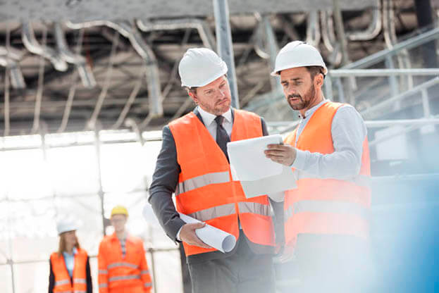 Engineers with blueprints and clipboard discussing paperwork at construction site